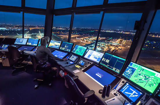 Air traffic controller working at a bank of screens in an airport tower at night